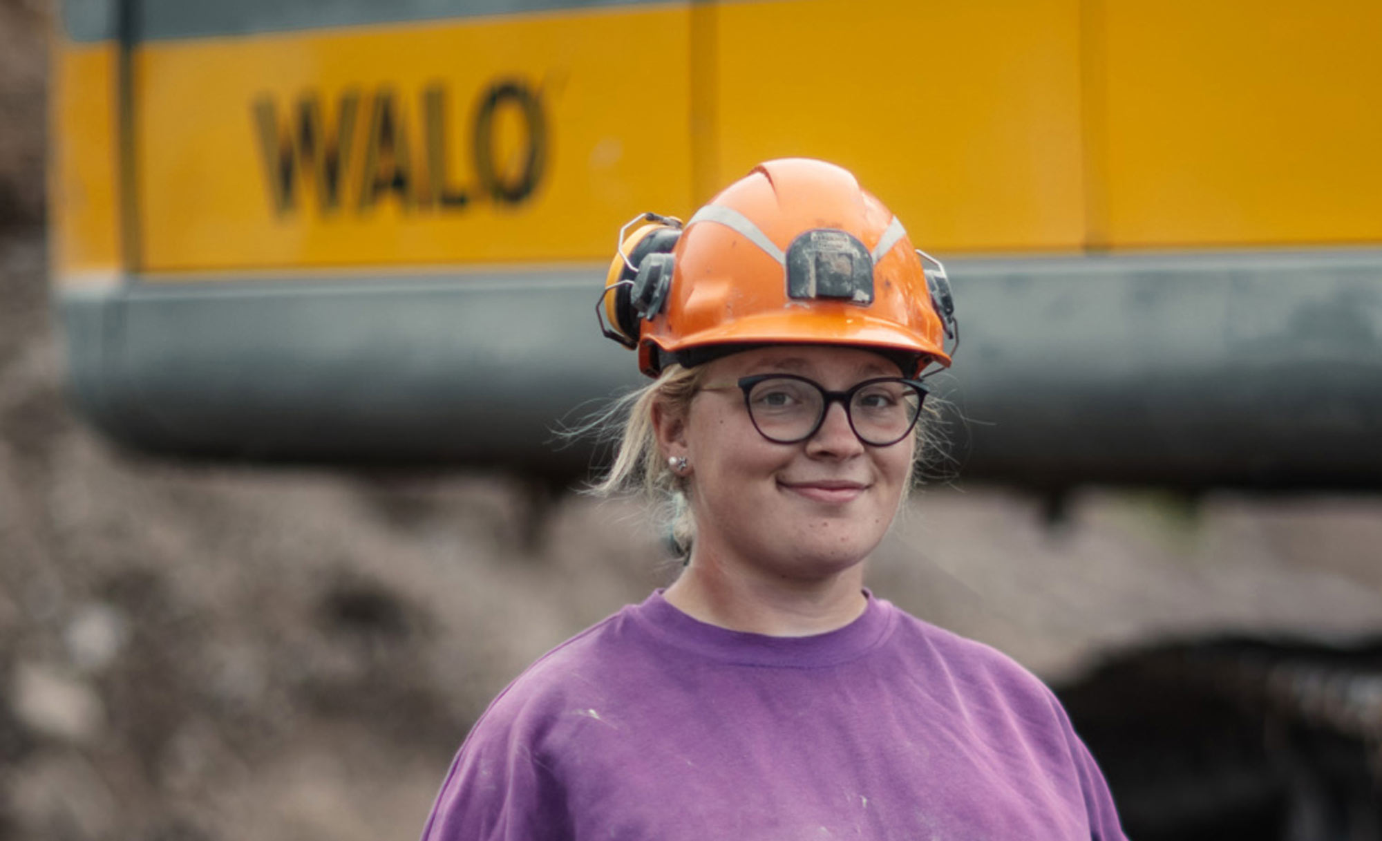Porträt einer jungen Frau mit orangem Schutzhelm auf einer Baustelle mit Maschinen